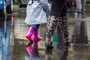 Dewsbury / Great Britain - May 2, 2016:  Legs of mother and child walking though the rain with wellies and rain boots on.  Reflections can be seen on the wet road pavement.