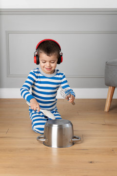 Little boy wearing headphones playing drums with pots and pans