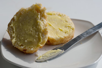 Cheese scone cut in two with butter on a small plate and knife.  Snack, baking, tasty, afternoon tea concepts.