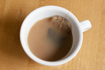 Looking down into a teacup or mug with tea inside including an individual teabag on string on a wooden table.  Tea, teabreak, cuppa tea concepts.