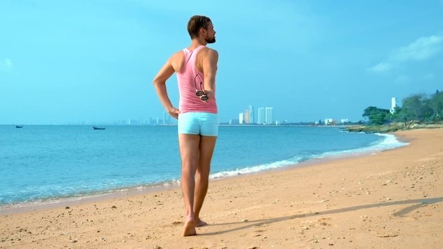 Playful handsome guy in a pink t-shirt and blue shorts rejoices at the beach. freak on the sea.