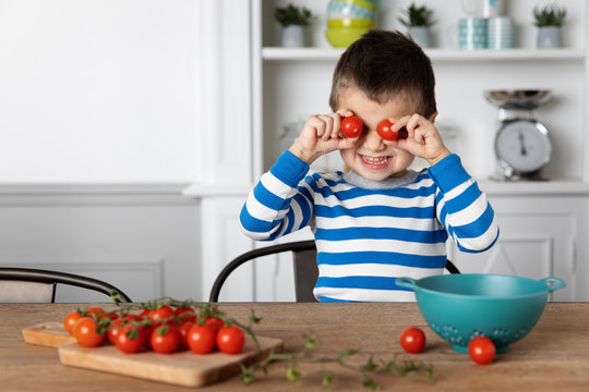 Smiling boy playing with cherry tomatoes at home