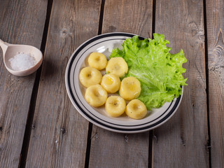 Cooked potato gnocchi, leaves of fresh leaf lettuce on a striped bright ceramic plate on an old plank table.