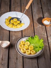 Potato gnocchi on two plates, leaves of fresh leaf lettuce on light plates on an old plank table. Near a wooden spoon with coarse salt.