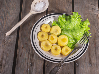 Ceramic plate with ready-made potato gnocchi with leaves of fresh leaf lettuce, on the plate lies a fork. Near wooden spoon with coarse white salt.