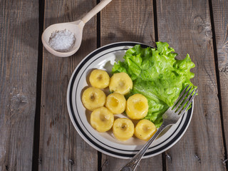 Ready-made potato gnocchi with leaves of fresh leaf lettuce on a ceramic plate with stripes, a table fork and a spoon on a plank rustic table.