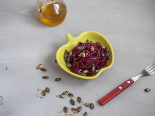 Vegetarian salad of grated boiled beets and seeds in a yellow ceramic salad bowl in the shape of an apple