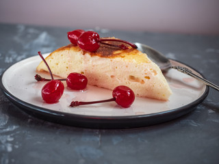 Portion of cottage cheese casserole on a ceramic saucer with a teaspoon, casserole decorated with canned cherries