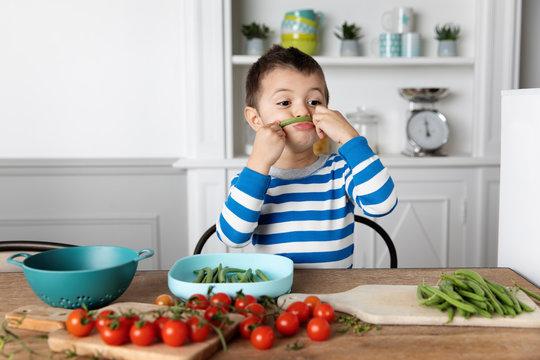 Boy making mustache with green bean at home