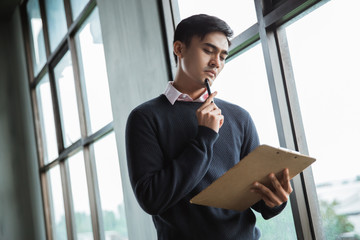 serious businessman thinking look on clipboard on his hands with put a ballpoint on the chin in the...