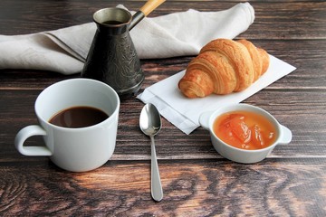 croissant, coffee, jam, napkin on a brown wooden background.
