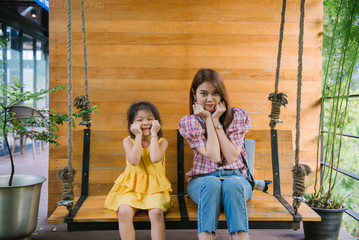 Happy family fun. Young mother and daughter playing on a swing in a nice cafe. Family weekend vacation.