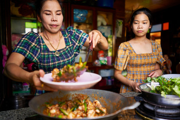 thai mother and daughter plating freshly cooked red curry in rustic traditional kitchen