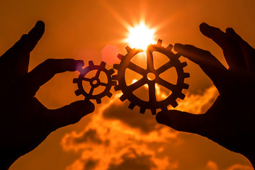 Gears in the hands of people against the sunset, the evening sky. the mechanism of interaction.