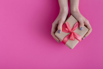girl holding a present in hands, women with gift box in hands wrapped in decorative craft paper with a tied red ribbon bow on colored cardboard background, top view, concept holiday, love and care