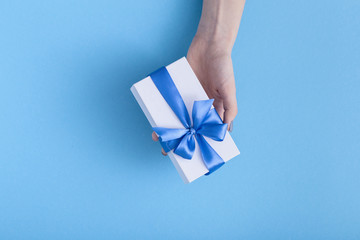girl holding a beautiful present in hands, women with gift box with a tied blue ribbon bow in hands on a pastel colored background, top view, concept holiday, love and care