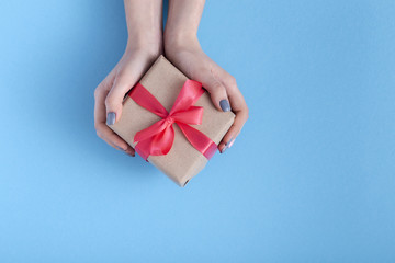 girl holding a present in hands, women with gift box with a tied red ribbon bow in hands on a pastel colored blue background, top view, concept holiday, love and care