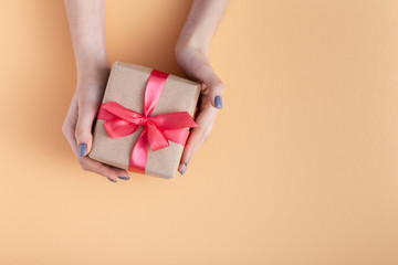 girl holding a present in hands, women with gift box in hands wrapped in decorative craft paper with a tied red ribbon bow on a pastel colored background, top view, concept holiday, love and care