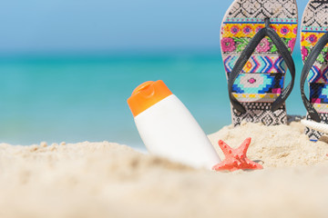 Protective sunscreen or sunblock and sunbath lotion in white plastic bottles with sandals on tropical beach, summer accessories in holiday, copy space.  Summer Concept