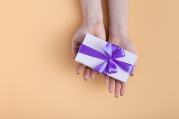girl stretch forward on the palms present, female with gift box with a tied lilac ribbon bow in hands on a pastel colored orange background, top view, concept holiday, love and care