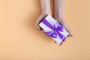 girl holding a present in hands, women with gift box with a tied lilac ribbon bow in hands on a pastel colored orange background, top view, concept holiday, love and care