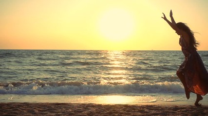 Beautiful girl jumping on the sea coast at sunrise