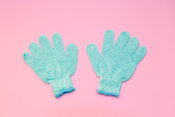 Bath massage blue gloves for shower with exfoliating hydro peeling scrub effect on soft pink background. Top view, flat lay.