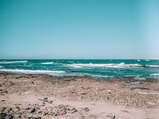 seashore with black stones and blue crystal clear water