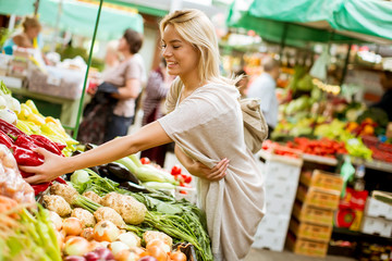 Cute young woman buying vegetables at the market