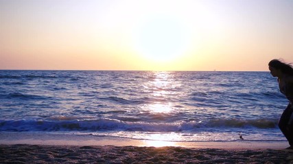 Beautiful girl jumping on the sea coast at sunrise