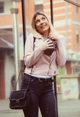 beautiful blond girl outside surprised and happy with gift bag in pink leather jacket smiling celebration concept  