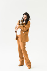 Full length view of pregnant woman in brown suit holding dog on white background