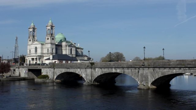 Cars and people moving across a bridge with a cathedral in the background.