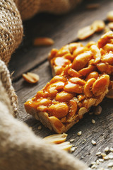 Sweets bar of peanuts on a vintage background with burlap. Delicious oriental sweets Gozinaki from sunflower seeds, sesame and peanuts, covered with honey with a shiny icing © Alexander