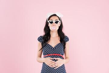 Brunette pregnant woman chewing bubble gum and touching belly isolated on pink
