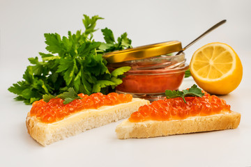 Two sandwiches with red caviar and butter on the background of a jar of caviar, lemon, parsley. Salmon caviar. Sea fish delicacy.