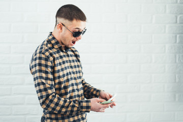 A man in a plaid shirt with a wad of money in his hands screaming with joy