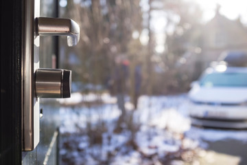 Chrome handle with a lock on the open metal front door, against the blurred background of the courtyard, in the bright rays of the spring sun.