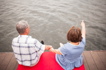 Elderly couple sit by the lake and hold hands