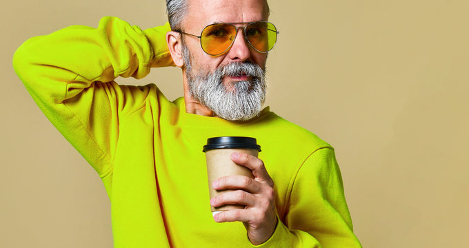 Vertical shot of a joyful senior holding a white coffee cup and looking at the camera