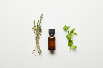 Top view of essential oil, thyme and fresh mint on white background