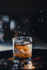ice cube falls into a glass with a cocktail. coke, whiskey and ice. Fluid in motion. Droplets of spray.