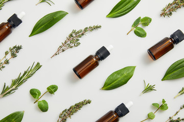 Flat lay with bottles on essential oil and green herbs on grey background