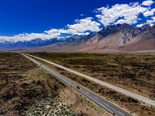 Fototapeta premium Aerial, drone view of Owens Valley and the snowcapped Eastern Sierra Nevada Mountains along California State Highway 395 in the spring with blue sky, white clouds, purple mountains and green flora