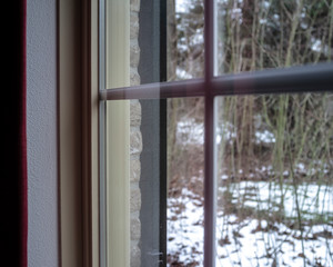 Window frame with a transparent double glazing and decorative elements inside the glass, in a brick house, against the background of a snow-covered yard and trees.