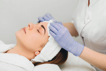 beautician wiping face to her patient before skin treatment
