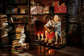 beautiful little girl in a blue dress like a princess is sitting on a toy wooden horse in a vintage studio.