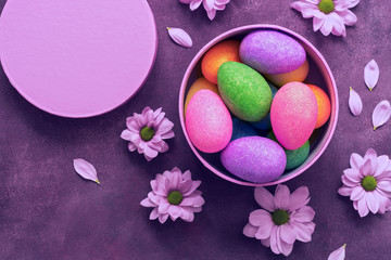 Colorful shiny Easter eggs in a round gift box on purple background decorated with flowers. Holiday Easter. Top view ,copy space