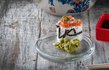 Japanese sushi rolls of rice avocado salmon soy sauce and sticks. serving on a light wooden table