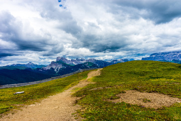 Alpe di Siusi, Seiser Alm with Sassolungo Langkofel Dolomite, a trekking walking winding path in a lush green fieldAlpe di Siusi, Seiser Alm with Sassolungo Langkofel Dolomite, a trekking walking wind
